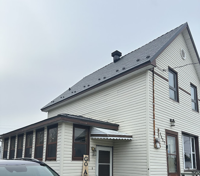 A two-story house with beige siding, a dark metal roof, and a small enclosed porch.