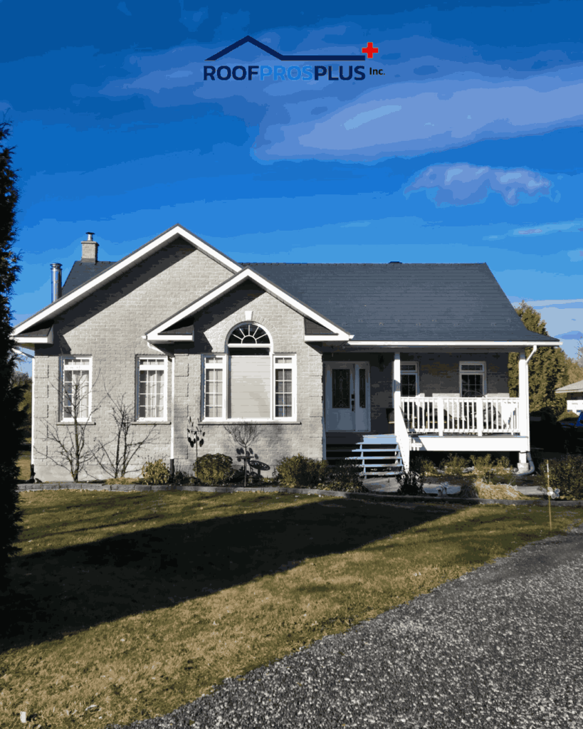 A single-story grey brick house under a clear blue sky, with a dark metal roof. The house has white trim, arched windows, and a small front porch.