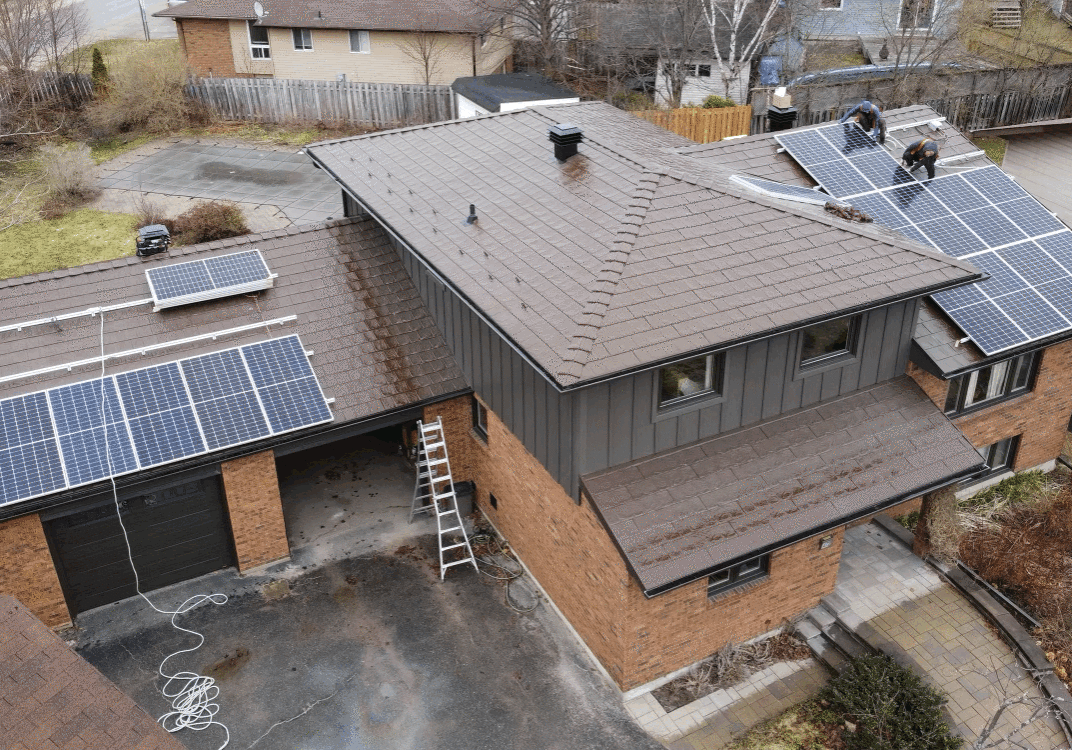 Aerial drone view of a suburban two-story brick house with a dark metal roof and newly installed solar panel system.