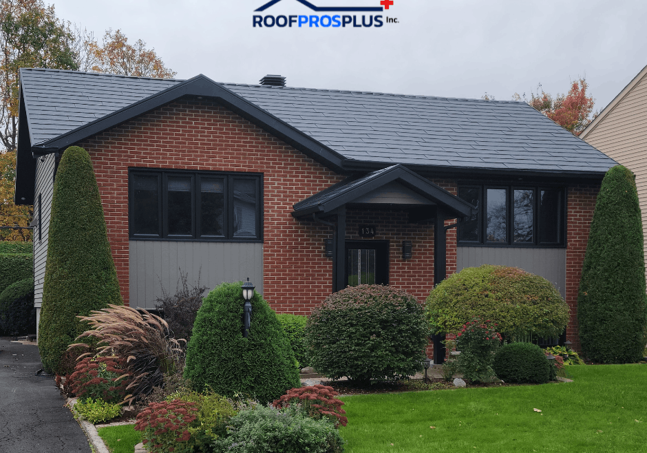 A brick house with a dark grey metal roof, surrounded by manicured shrubs and green lawn. Logo "Roof Pros Plus Inc." is at the top of the image. Autumn trees in the background.