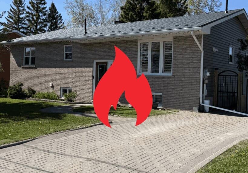 A modern house with a grey metal roof and brick exterior, featuring a green lawn and a paved driveway, with a fire symbol overlay.