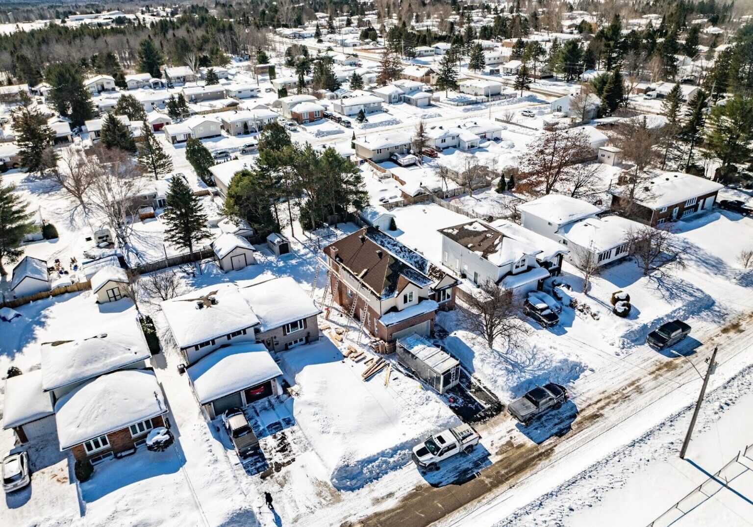 Aerial view of a snowy suburban neighbourhood with tree-lined streets and houses blanketed in snow, capturing a peaceful winter scene.