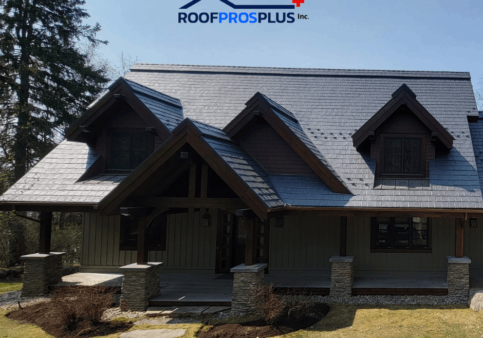 A cozy cottage-style house with a steep, triangular metal roof and wooden beams is surrounded by trees and a lush lawn.