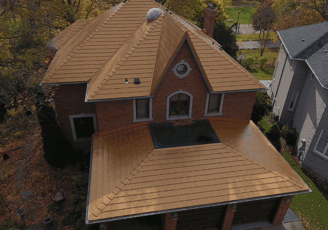 Aerial view of a two-story red brick house with a copper-toned metal roof, surrounded by autumn trees. The "Roof Pros Plus Inc." logo is at the top right.