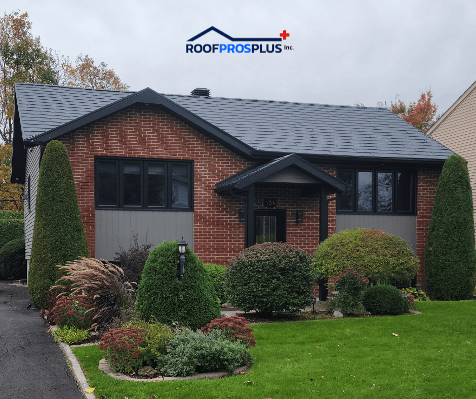 A brick house with a dark grey metal roof, surrounded by manicured shrubs and green lawn. Logo "Roof Pros Plus Inc." is at the top of the image. Autumn trees in the background.