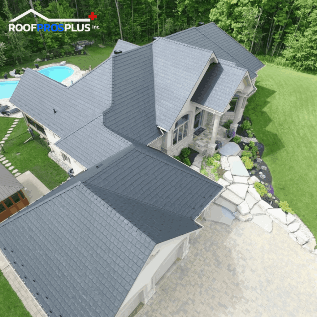 An aerial view of a large house with a dark grey metal roof, surrounded by lush greenery. A stone pathway and pool are in the backyard. The Roof Pros Plus logo is at the top left corner of the image.