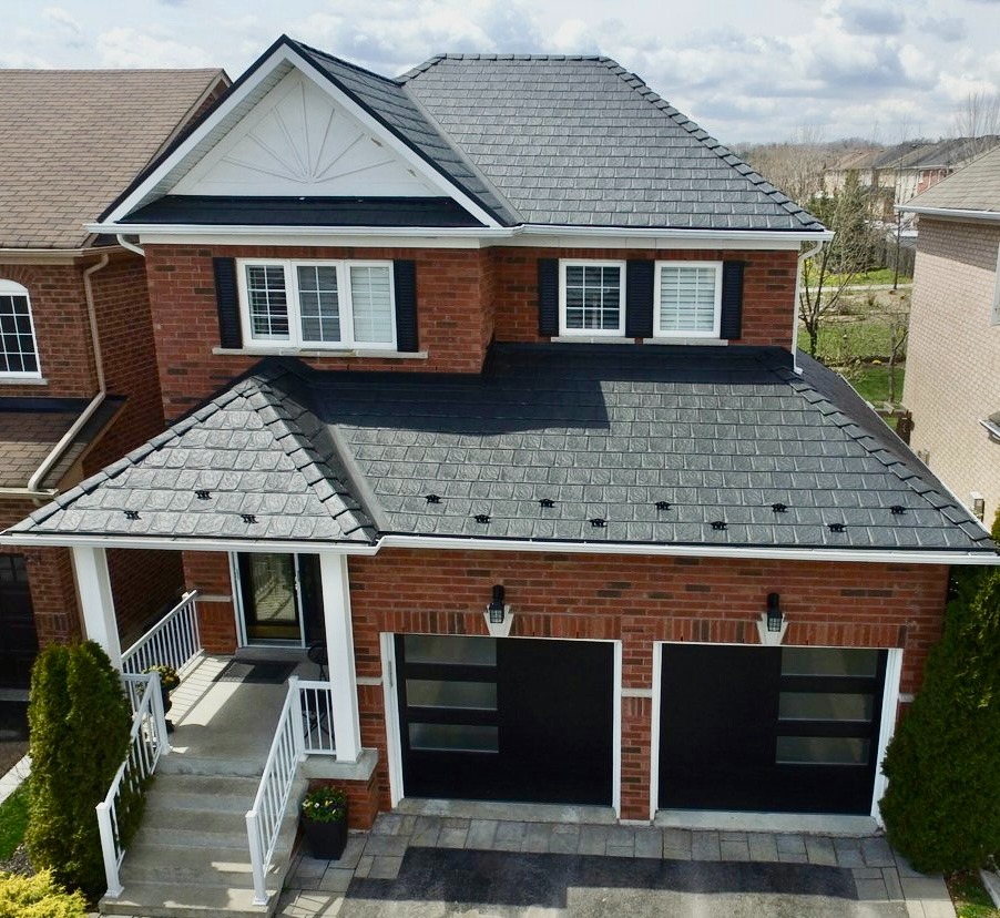 A two-story red brick house with a dark gray metal roof, white trim, and black shutters. The house has two black garage doors and a small porch.