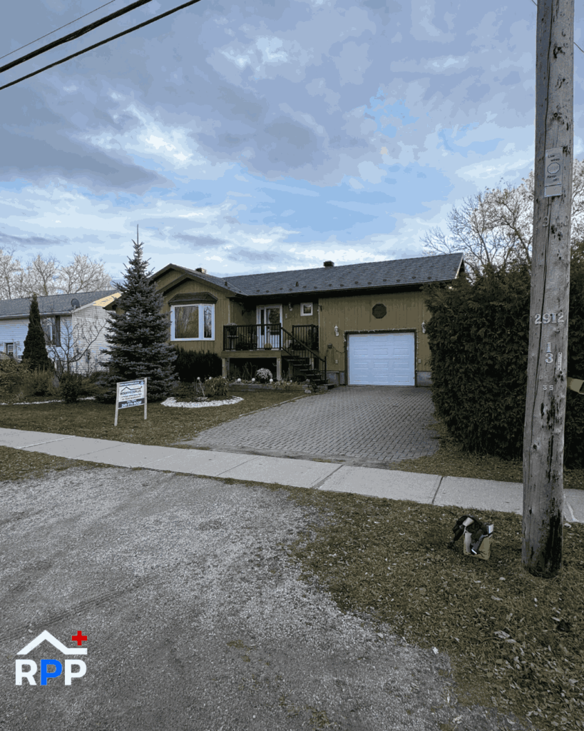 Front view of a single-storey home with a dark metal roof, attached garage, and paved driveway. A Roof Pros Plus sign is displayed on the front lawn, with trees, neighbouring homes, and a cloudy sky in the background.
