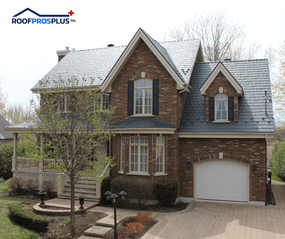 A brick home with a grey metal roof by Roof Pros Plus, featuring dormers, a covered porch, and landscaped yard.