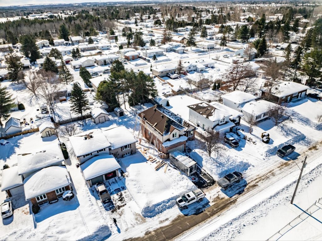Aerial view of a snowy suburban neighbourhood with tree-lined streets and houses blanketed in snow, capturing a peaceful winter scene.