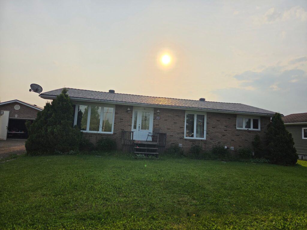 A single-story brick house with a newly installed metal roof and a grassy front lawn and shrubs.
