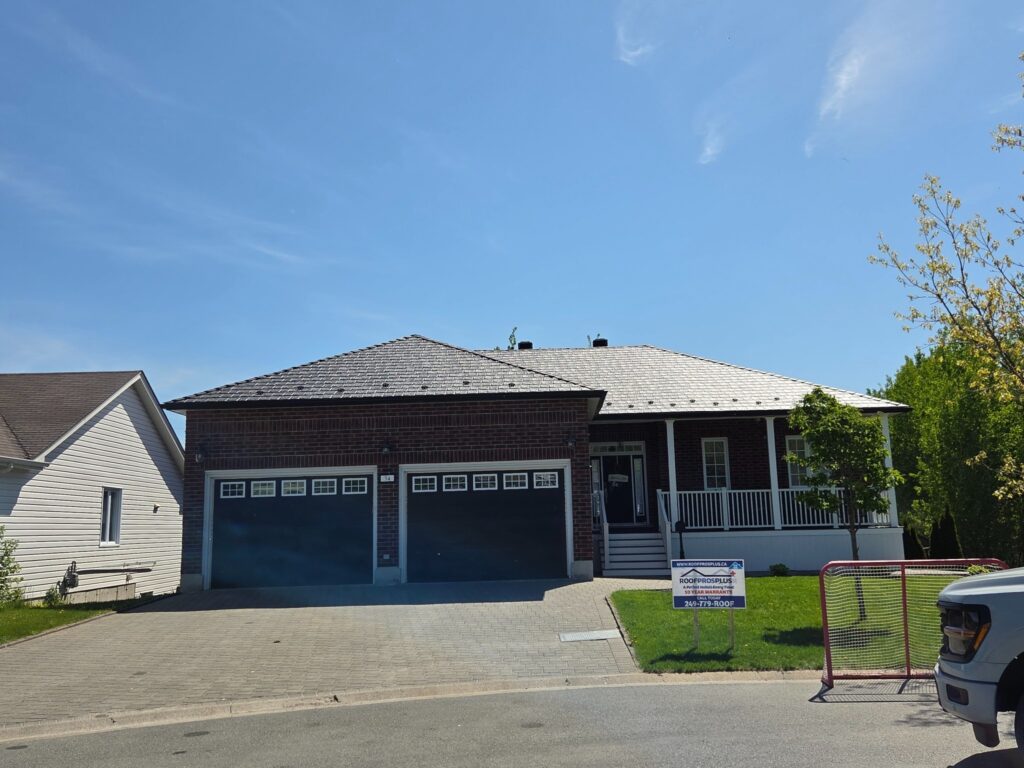 A single-story brick house with a double garage and porch is set under a blue sky. A Roof Pros Plus sign and hockey net are at the front of the house. 