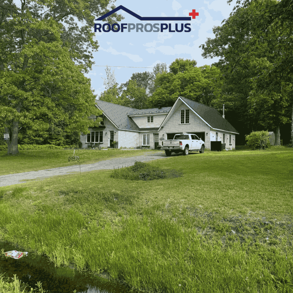 A white house with a dark metal roof is surrounded by trees and greenery. A white truck is parked on the gravel driveway. The scene is peaceful and rural. Logo text reads "ROOFPROSPLUS" at the top.
