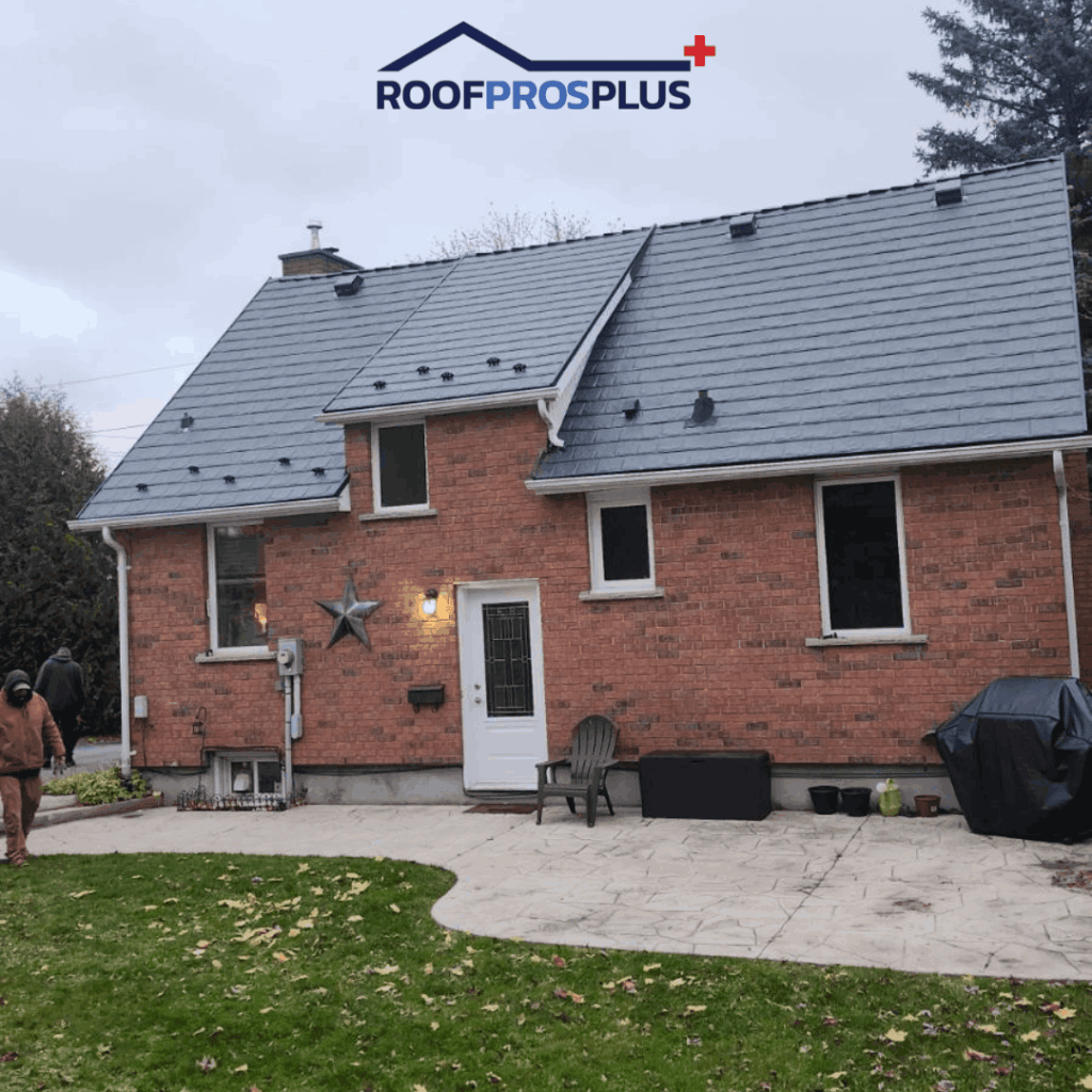 A brick house with a new grey metal roof. The patio has a chair and grill, with a leaf-strewn lawn. 