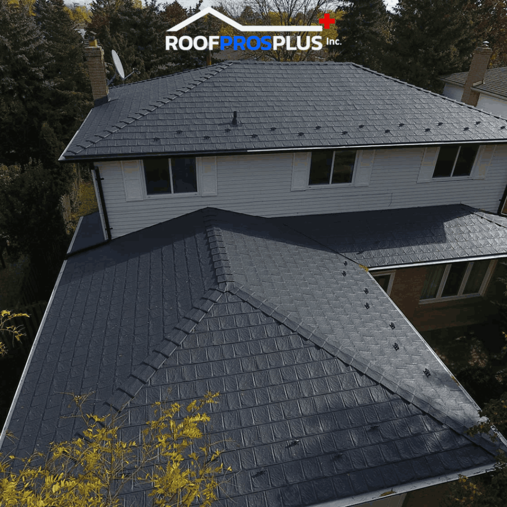 A two-story house features a new dark grey metal roof under a cloudy sky. Tall trees surround the house.