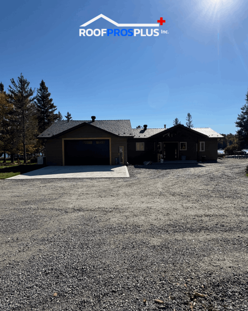 A modern, single-story house with a grey metal roof, two garage doors, and a gravel driveway. It's sunny with clear skies and surrounded by trees. The Roof Pros Plus logo is at the top of the graphic.