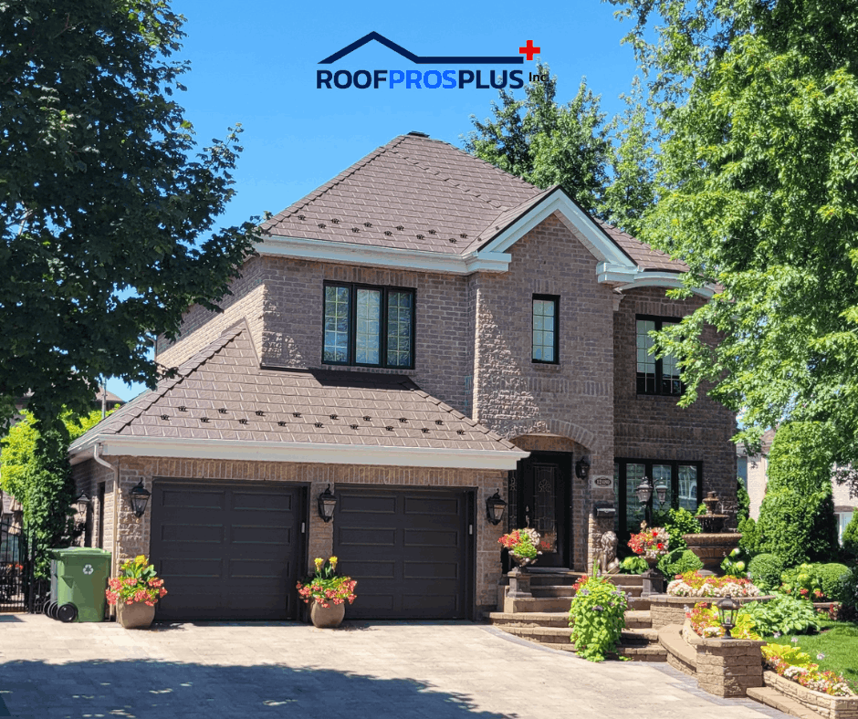 A brick two-story house with dark garage doors, framed by lush trees and vibrant flower pots.