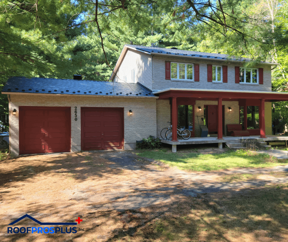 A two-story house with a grey brick exterior, red shutters, and a matching red garage and porch. The house is surrounded by green trees.