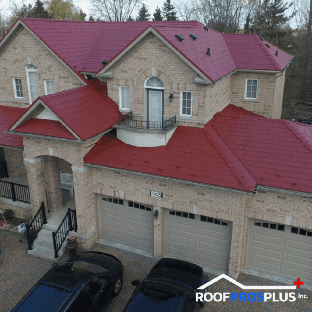 A large brick house with a vivid red metal roof, multiple garages, and a black car parked in front. The Roof Pros Plus logo is in the bottom right hand corner.