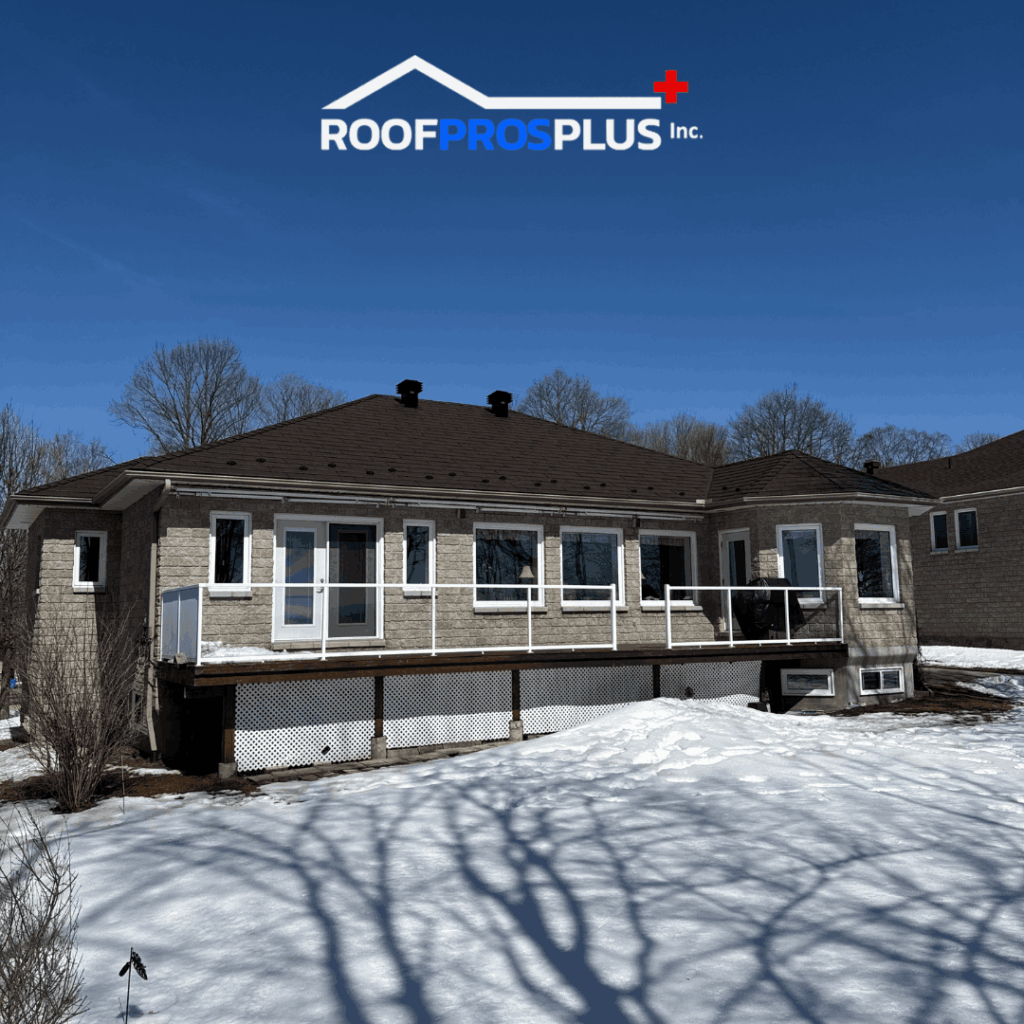 A modern house with a brown metal roof sits against a clear blue sky. The snow-covered yard creates a crisp contrast. The RoofProsPlus Inc.logo is at the top of the image.